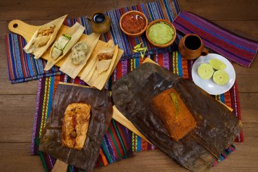 Variedad de tamales guatemaltecos: tamales colorados, paches de papa y chuchitos servidos en mesa tradicional.